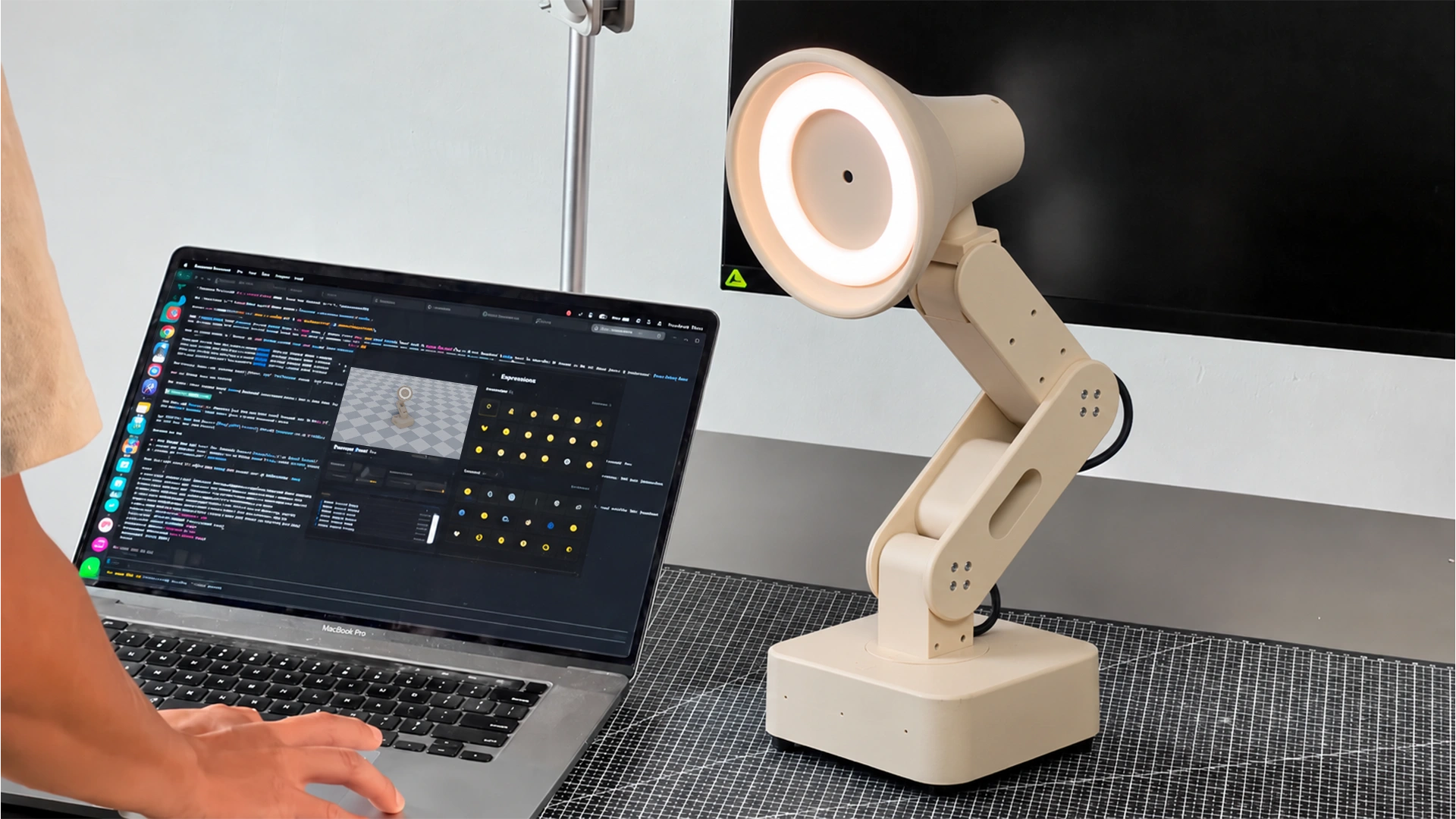 A researcher at a laptop works on Lamp’s gestures while Lamp tilts its lit head beside them