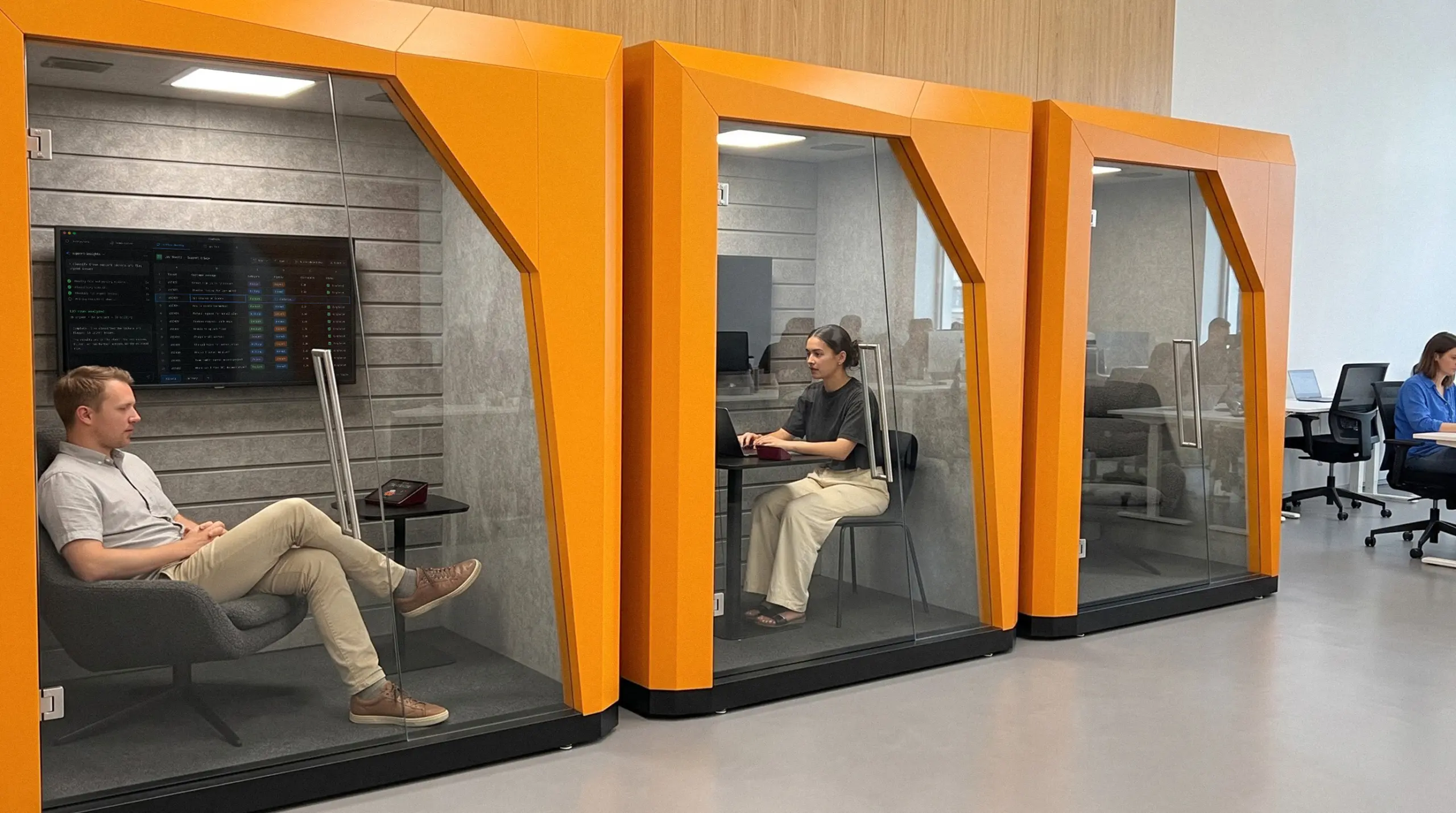 Three FocusPods in a row on an office floor: one man talking to agents, one woman on a laptop call, one pod free