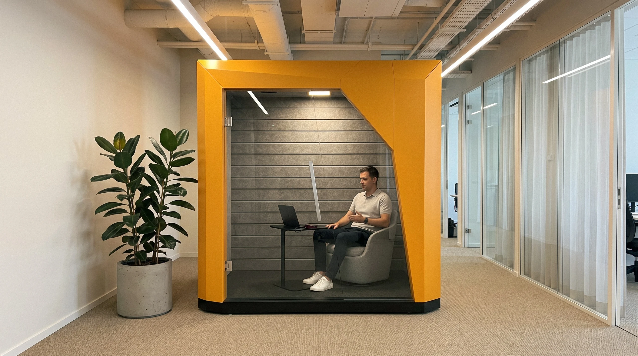 A man on a video call on his laptop inside FocusPod, the laptop table pulled over his lap, the big screen off